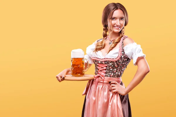 Giovane ragazza sexy Oktoberfest cameriera, indossa un abito tradizionale bavarese, che serve grandi tazze di birra su sfondo arancione con spazio copia . — Foto Stock