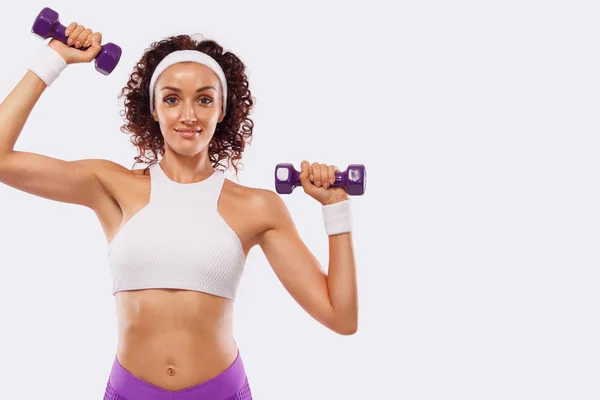 Sporty beautiful woman with dumbbells makes fitness exercising at white background to stay fit — Stock Photo, Image