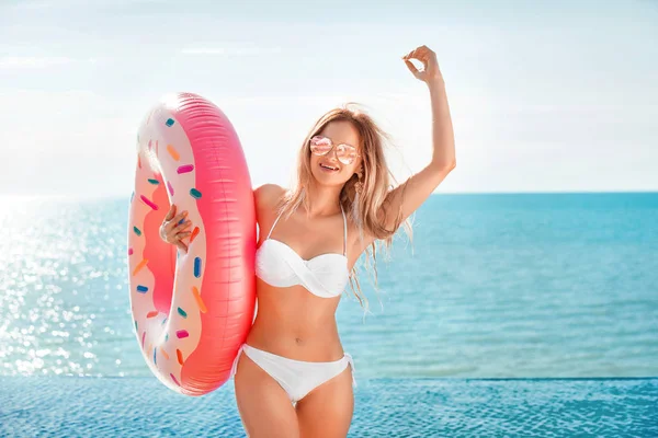 Vacaciones de verano. Disfrutando de una mujer bronceadora en bikini blanco con colchón de rosquillas cerca del océano . — Foto de Stock