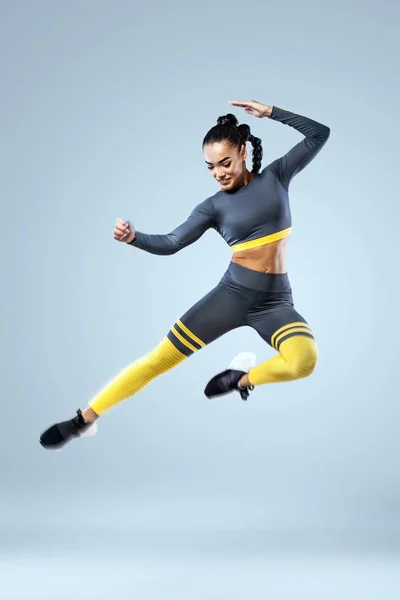 Attractive excited fitness girl dancer in sportwear jumping of joy isolated over gray background — Stock Photo, Image