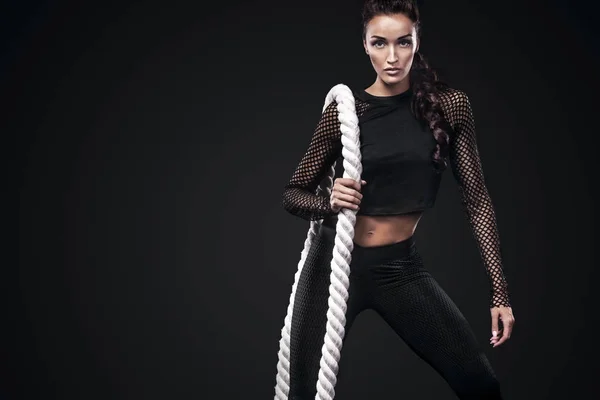 Mulher bonita desportiva com corda de batalha faz exercício de fitness em fundo preto para ficar em forma — Fotografia de Stock