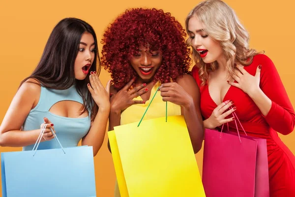 Drei überraschten Frauen nach dem Einkaufen. Afroamerikanische, asiatische und kaukasische Rassen. orangefarbener Hintergrund am schwarzen Freitag. Konzept für Verkaufswerbung. Double-Elfer-Einkaufsfest . — Stockfoto