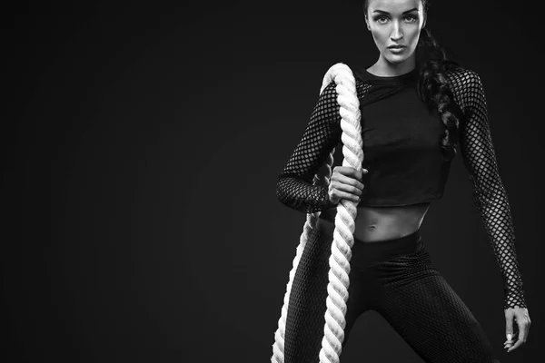 Спортивная красивая женщина с боевой веревкой делает фитнес упражнения на черном фоне, чтобы оставаться в форме — стоковое фото