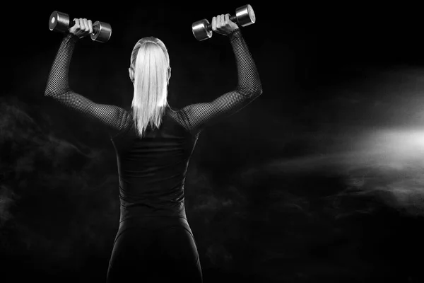 Mulher bonita desportiva com halteres faz exercício de fitness em fundo preto para ficar em forma — Fotografia de Stock