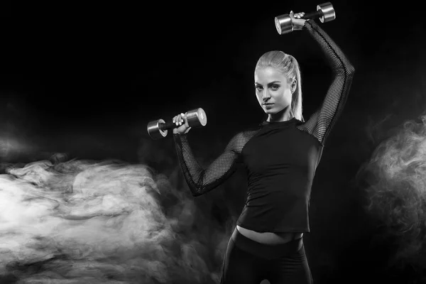 Спортивная красивая женщина с гантелями делает фитнес упражнения на черном фоне, чтобы оставаться в форме — стоковое фото