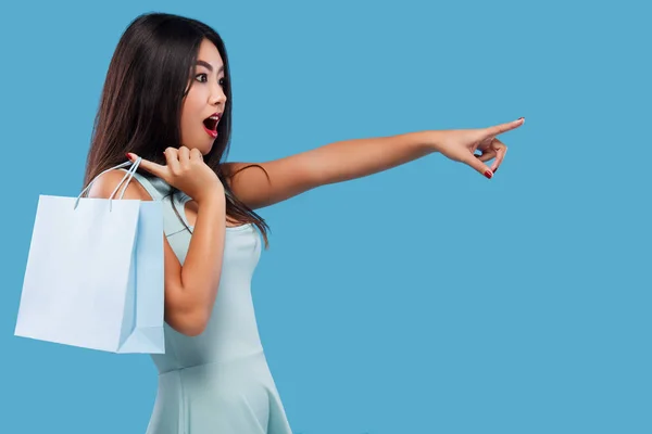 Förvånad över asiatisk kvinna på shopping innehav väska och punkter upp på kopia utrymme. Isolerad på blå bakgrund på svart fredag semester. — Stockfoto