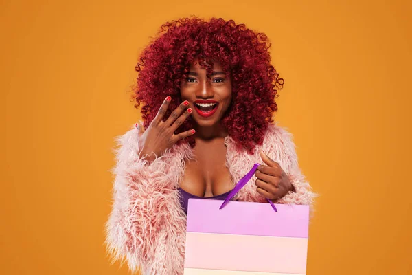 オレンジ色の背景に黒い金曜日休日に分離されたピンクのバッグを持ってショッピングでアフロ ・ アメリカ人女性。販売の広告のためのスペースをコピーします。. — ストック写真