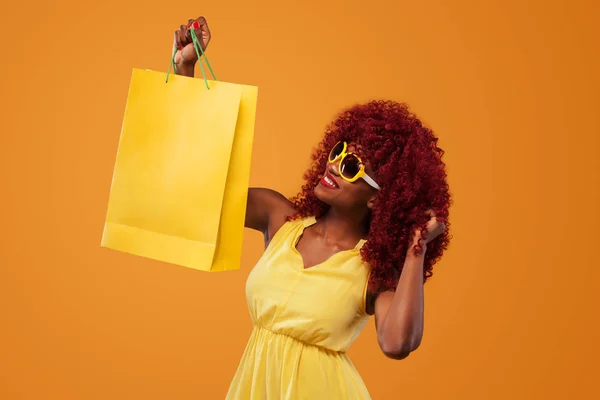 Femme afro-américaine au salon du shopping sur sac jaune isolé sur fond orange le vendredi noir vacances. Espace de copie pour la vente annonces . — Photo