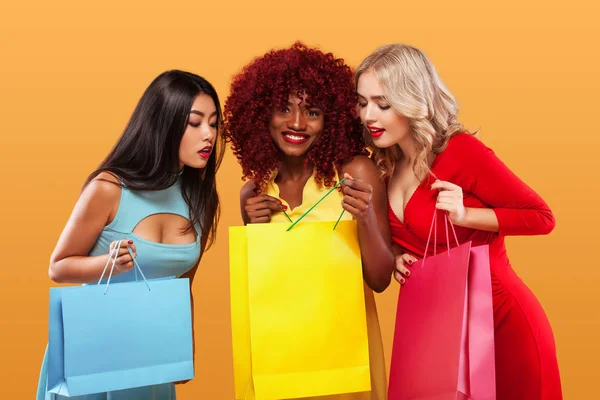 Groupe de femmes surprises après les courses. Afro-américains, asiatiques et caucasiens. Fond orange pendant les vacances du vendredi noir. Concept à vendre publicité. Double Eleven Shopping Festival  . — Photo