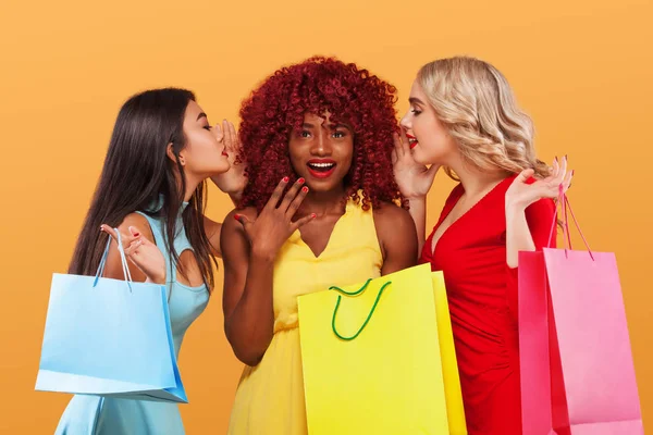 Trois femmes heureuses après les courses. Afro-américains, asiatiques et caucasiens. Shopping avec isolé sur fond orange pendant les vacances du vendredi noir. Concept de vente publicité . — Photo