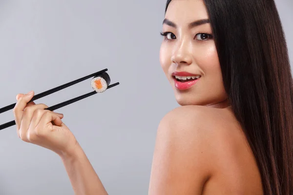 Asian woman eating sushi and rolls on a gray background. Copy space.
