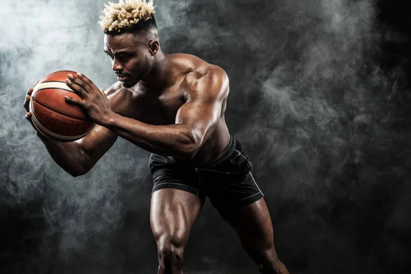 Retrato de desportista afro-americano, jogador de basquetebol com uma bola sobre fundo preto. Ajuste jovem em sportswear segurando bola . — Fotografia de Stock