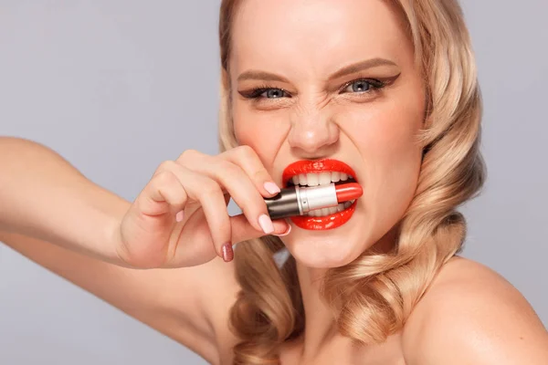 Close up portrait of attractive girl rouging her lips. She is holding red lipstick in the mouse. Isolated on gray background with copy space — Stock Photo, Image