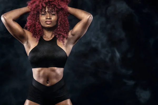 Спортивная красивая афро-американская модель, женщина в спортивной форме делает фитнес упражнения на черном фоне, чтобы оставаться в форме — стоковое фото