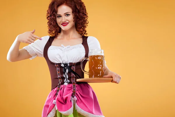 Fiatal szexi Oktoberfest pincérnő, egy hagyományos bajor ruhát viselt sárga alapon nagy söröskorsót szolgáló. — Stock Fotó