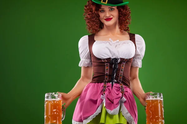 St Patricks Day. Ung sexig Oktober fest servitris, bär en traditionell bayersk klänning, som serverar stora ölglas på grön bakgrund med kopia utrymme — Stockfoto