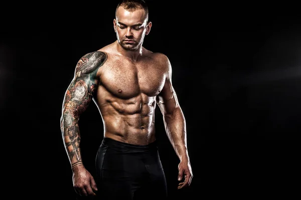 Bonito homem em forma posando usando jeans com tatuagem. Esporte e conceito de moda isolado no fundo preto . — Fotografia de Stock