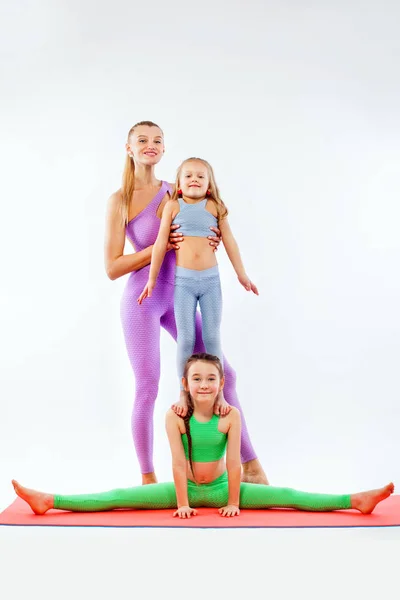 Hatha yoga fitness. Madre joven Instructor e hijas ejercen gimnasia juntos. Aislado sobre fondo blanco. Aspecto familiar . — Foto de Stock