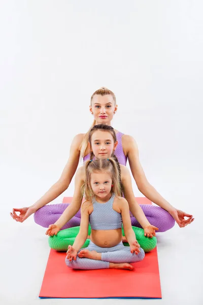 Йога Хатха. Дети фитнес. Молодая мама инструктор и дочери занимаются гимнастикой вместе. Изолированный на белом фоне. Семейный взгляд . — стоковое фото