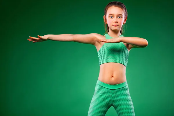 Дитяча дівчинка робить фізичні вправи на зеленому фоні — стокове фото