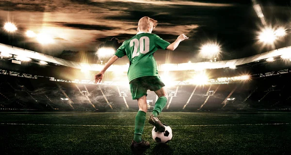 Kind - Fußballer. Junge vorwärts in Fußballsportbekleidung auf Stadion mit Ball. Sportkonzept. — Stockfoto