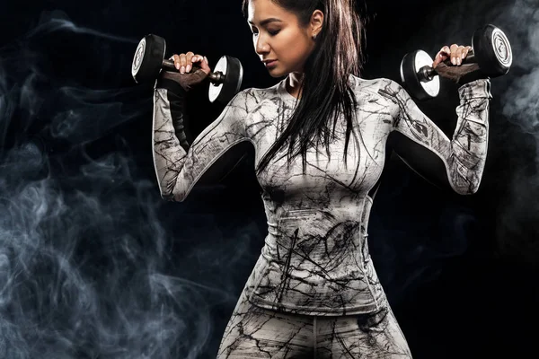 Sporty bella donna con manubri rende fitness esercizio su sfondo nero per rimanere in forma — Foto Stock
