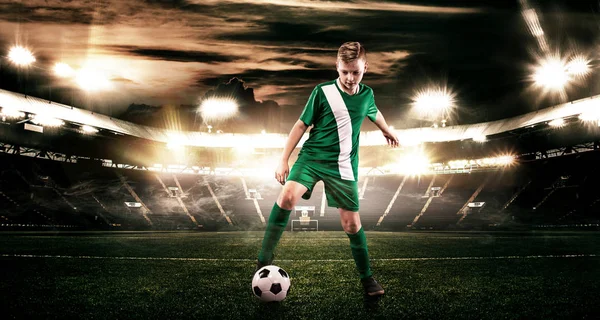 Kind - Fußballer. Junge vorwärts in Fußballsportbekleidung auf Stadion mit Ball. Sportkonzept. — Stockfoto