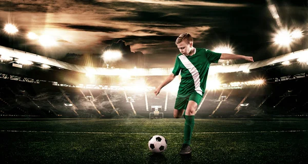 Kind - Fußballer. Junge vorwärts in Fußballsportbekleidung auf Stadion mit Ball. Sportkonzept. — Stockfoto