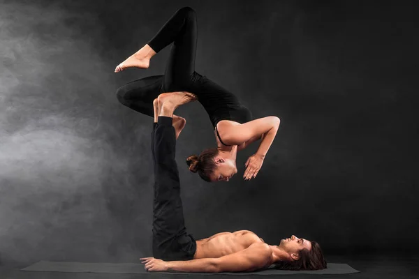 Acroyoga. Νεαρό ζευγάρι εξάσκηση acro yoga σε χαλί στο στούντιο μαζί. Γιόγκα ζευγάρι. Γιόγκα συνεργάτη. Μαύρο και άσπρο φωτογραφία. — Φωτογραφία Αρχείου