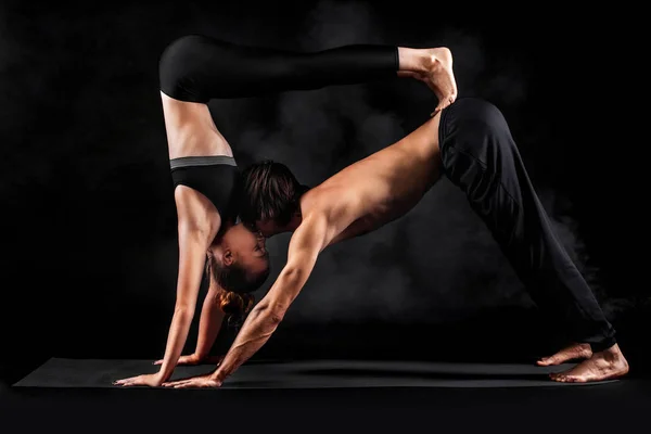 Acroyoga. Νεαρό ζευγάρι εξάσκηση acro yoga σε χαλί στο στούντιο μαζί. Γιόγκα ζευγάρι. Γιόγκα συνεργάτη. Μαύρο και άσπρο φωτογραφία. — Φωτογραφία Αρχείου