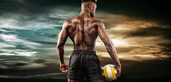 Ritratto di sportivo afro-americano, giocatore di pallavolo con palla sopra il cielo al tramonto. In forma giovane uomo in abbigliamento sportivo tenendo palla . — Foto Stock