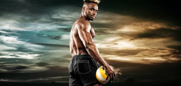 Porträtt av afro-american sportsman, volleybollspelare med en boll över himlen sunset. Passar ung man i sportkläder hålla bollen. — Stockfoto