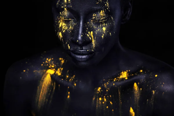Woman with black body paint. Cheerful young african girl with art  bodypaint. An amazing model with yellow makeup. Closeup face. Stock Photo