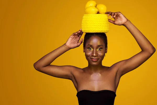 Vrolijke jonge Afrikaanse vrouw met gele make-up op haar ogen. Vrouwelijke model tegen een gele achtergrond met gele citroenen. — Stockfoto