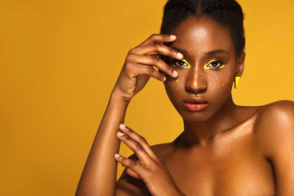 Jovem mulher africana alegre com maquiagem amarela nos olhos. Modelo feminino rindo contra fundo amarelo . — Fotografia de Stock