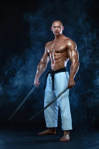 Samurai homem sem camisa com espada japonesa. Caça de karaté em fundo preto com fumo. Bonito e apto homem desportistas fisiculturista físico e atleta. Motivação desportiva masculina . — Fotografia de Stock