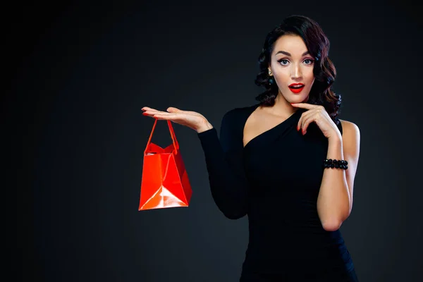 Fekete pénteki vásár koncepció a boltnak. Bevásárló lány kezében piros táska elszigetelt sötét háttérrel. A nő balra mutat a fénymásolón.. — Stock Fotó
