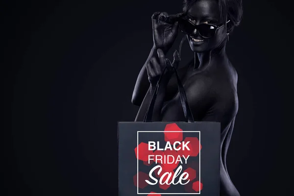 Svart fredag försäljning koncept för butik. Shopping kvinna med bodyart och ansikte konst innehav väska isolerad på mörk bakgrund i semester. — Stockfoto