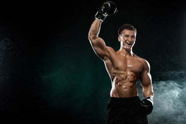 Boksör, boksör galibi ve şampiyon siyah arka planda eldivenlerle kusursuz zaferi kutluyor. Fitness ve boks konsepti. Bireysel spor eğlencesi.