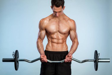 Vücut geliştirme sporcusu. Güçlü, kaslı, atletik bir adam hafif arka planda halterle kaslarını şişiriyor. Vücut geliştirme konsepti.