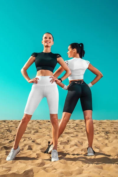 Duas jovens desportistas mulheres, atletas em forma estão de pé no fundo do céu antes de correr. Estilo de vida saudável e esporte. Amigos de sportswear preto e branco. Conceito de aptidão . Imagem De Stock