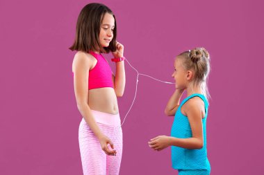 İki çocuk kız pembe arka planda müzik dinler. Çocuk yaşam tarzı konsepti.