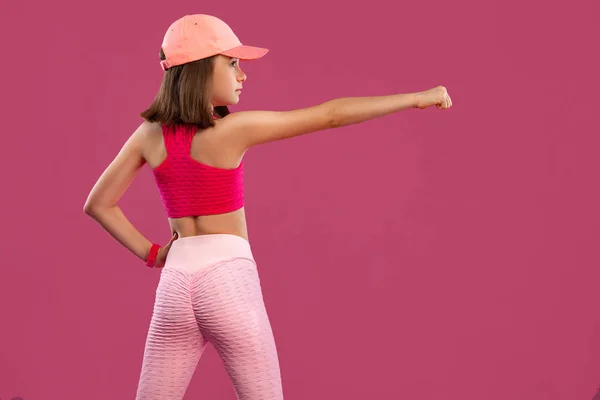 Sports concept. Kid girl doing fitness exercises on green and pink background in sportswear. — 스톡 사진