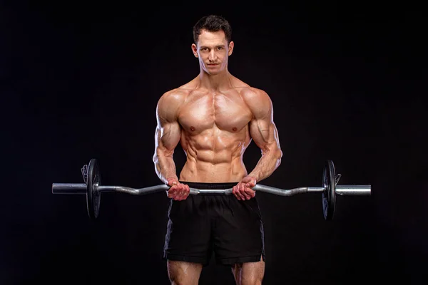 健美运动员。 粗野强壮的肌肉运动员在黑色背景上用杠铃抽吸肌肉。 锻炼身体的概念. — 图库照片