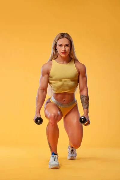 Vücut geliştirme sporcusu. Steroid kullanan güçlü atletik kadın, sarı arka planda dambılları olan spor kıyafetleri giyen. Spor ve spor motivasyonu. — Stok fotoğraf