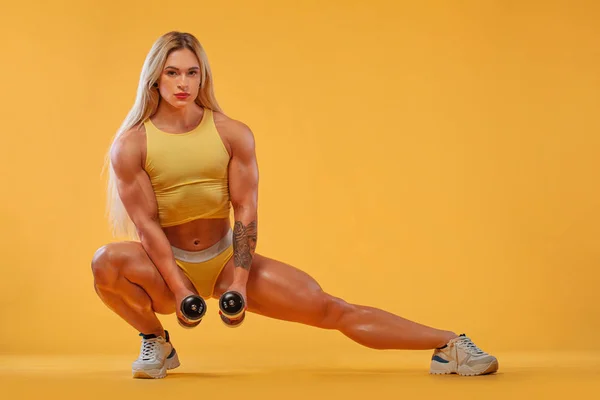 Idrottare kroppsbyggare. Stark atletisk kvinna på steroider med hantlar på gul bakgrund bär i sportkläder. Fitness och idrottsmotivation. — Stockfoto