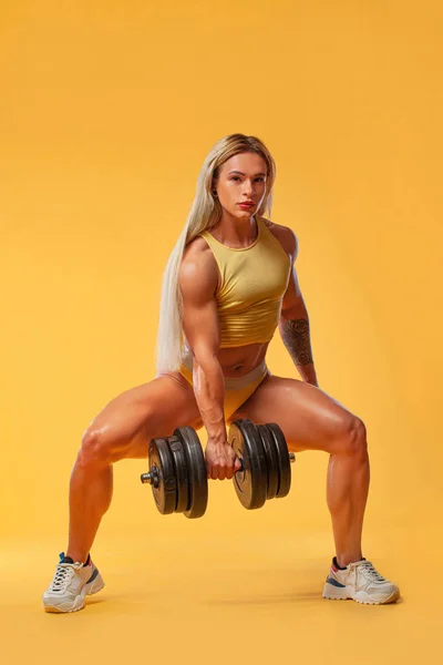 健美运动员。 强壮的女运动员穿着运动服，戴着黄色背景的哑铃，服用类固醇。 健身和运动动机. — 图库照片