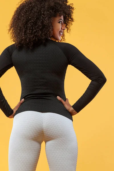 黒い肌と巻き毛の強い運動女性の背中、赤いスポーツウェアを着て黄色の背景に運動を行う。フィットネスとスポーツの動機. — ストック写真