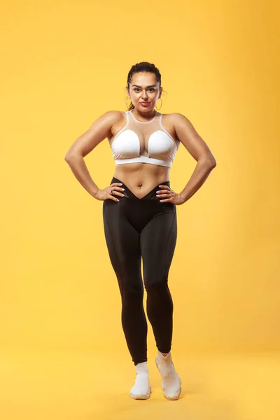 Méret plusz női sportos fitt nő sportruházatban, sportoló teszi fitness gyakorló sárga háttér. A kövér emberek motivációja. — Stock Fotó