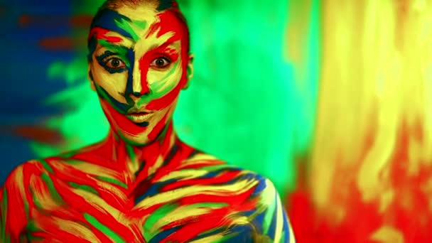 Color face art and body paint on woman in slowmotion. Abstract portrait of the bright beautiful girl with colorful make-up and bodyart. Cheerful woman showing wow emotion. — Stock Video